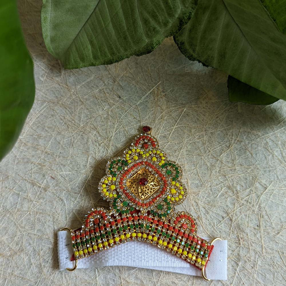 A 4-inch stone-studded Mukut with vibrant green, yellow, and red stones, designed for adorning deity idols.