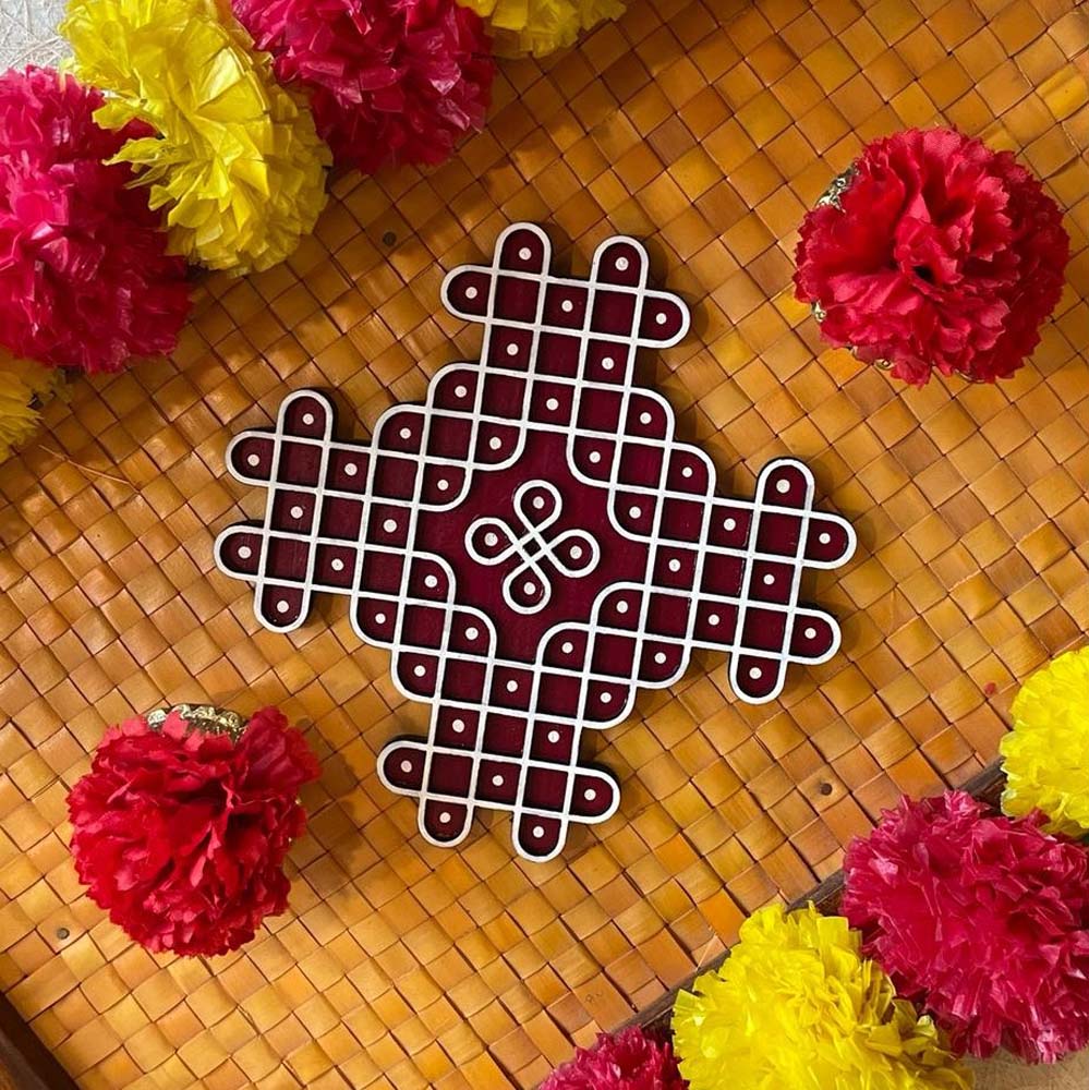 Handcrafted Pulli Arakku Kolam with a red base and intricate white grid design, surrounded by red and yellow floral garlands.