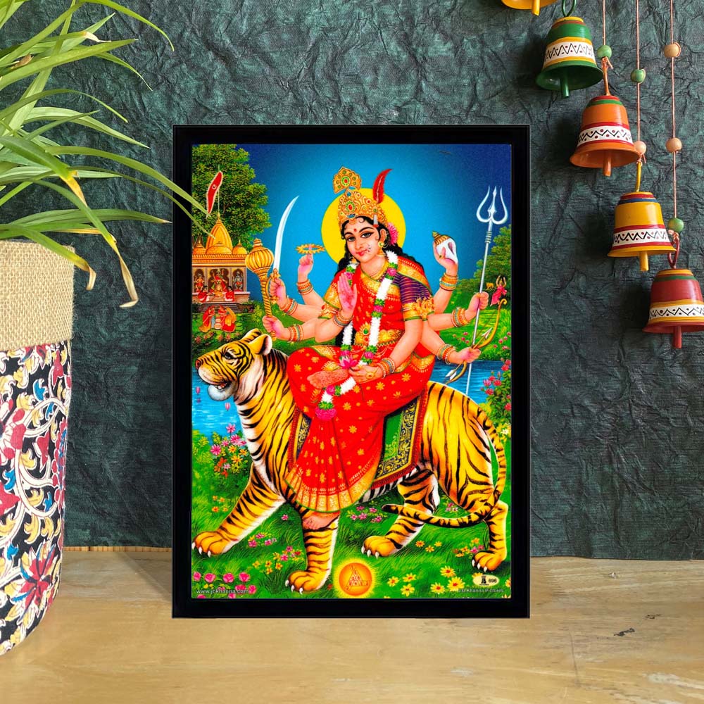 Goddess Durga seated on a tiger, holding weapons, with a vibrant background of temples and nature – framed art for home décor.