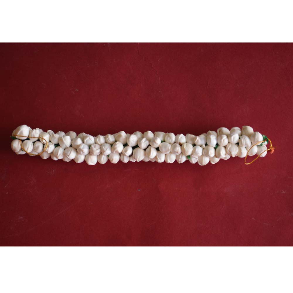 Handcrafted white Konda flower garland with green accents placed on a woven basket, perfect for hair decoration