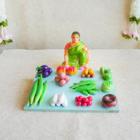 Navarathri Golu Doll of a seated vegetable vendor surrounded by an assortment of vibrant vegetables, hand-painted and crafted.