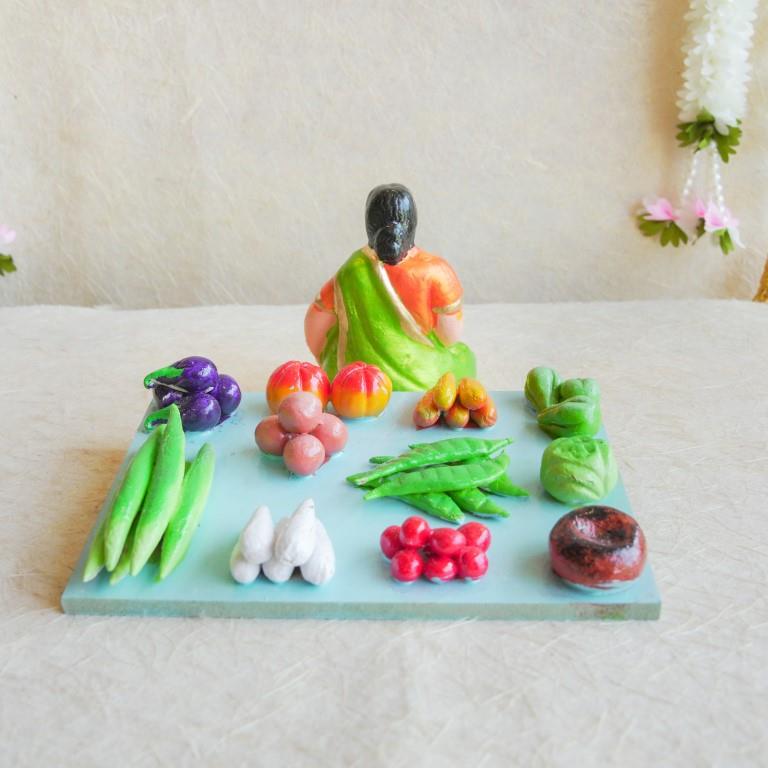Navarathri Golu Doll of a seated vegetable vendor surrounded by an assortment of vibrant vegetables, hand-painted and crafted.