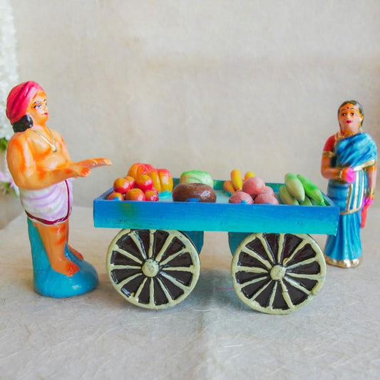 Navarathri Golu doll set featuring a vegetable seller with a cart filled with colorful fruits and vegetables, accompanied by a traditionally dressed woman in a blue saree.