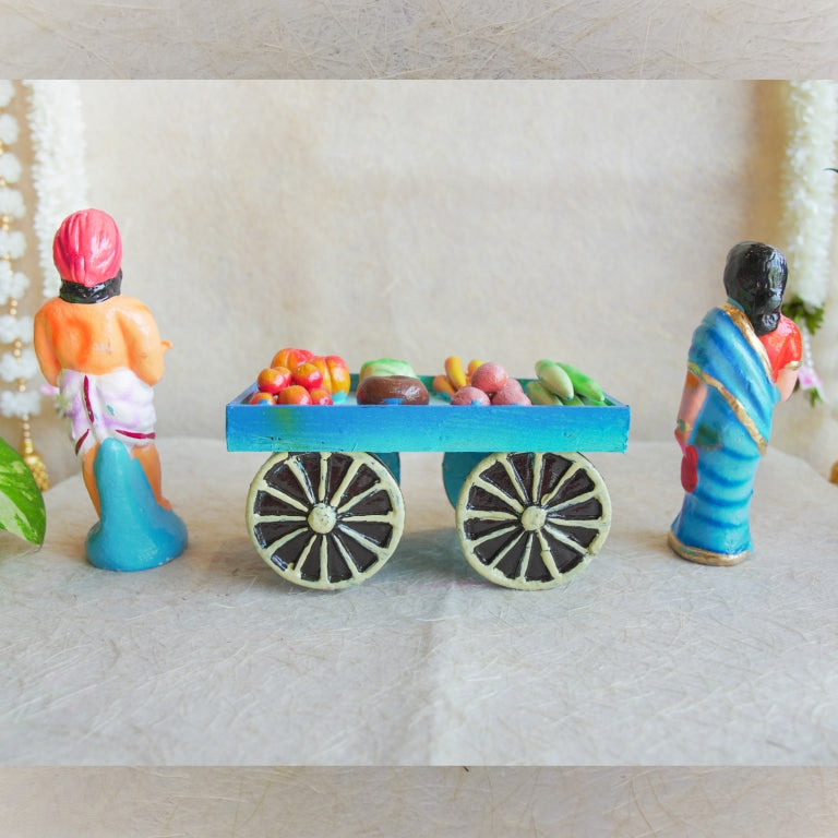 Navarathri Golu doll set featuring a vegetable seller with a cart filled with colorful fruits and vegetables, accompanied by a traditionally dressed woman in a blue saree.