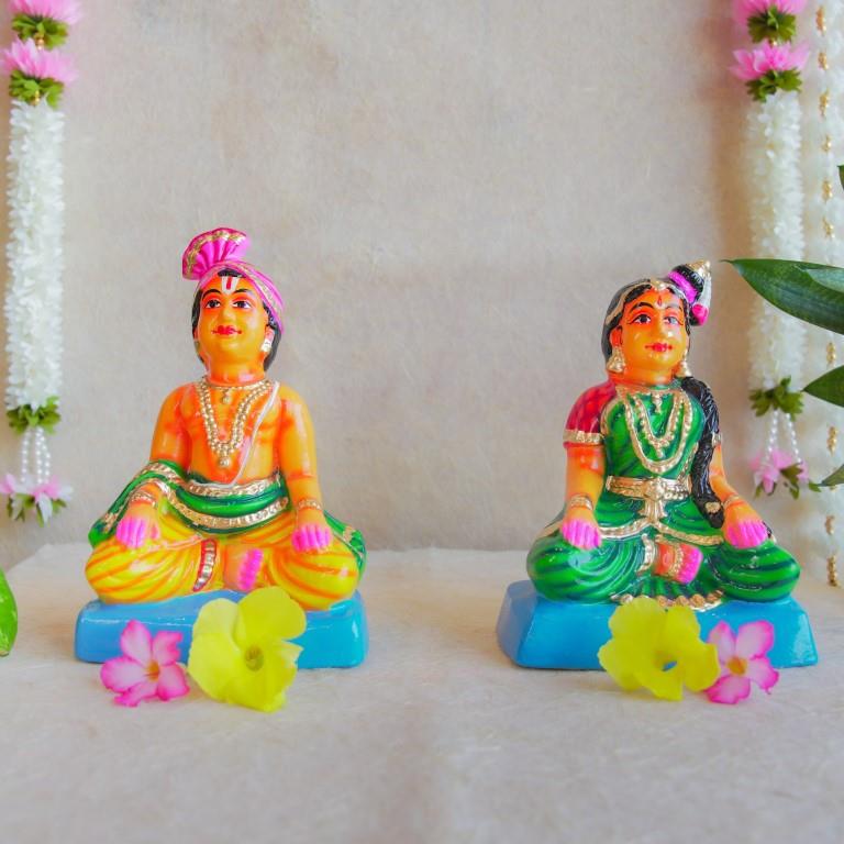 Navarathri Golu dolls depicting a seated Mama and Mami, dressed in traditional attire with vibrant colors, sitting on blue bases.