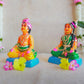 Navarathri Golu dolls depicting a seated Mama and Mami, dressed in traditional attire with vibrant colors, sitting on blue bases.