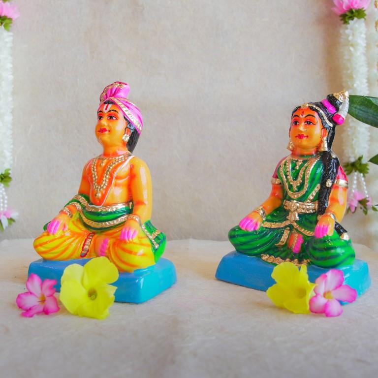 Navarathri Golu dolls depicting a seated Mama and Mami, dressed in traditional attire with vibrant colors, sitting on blue bases.