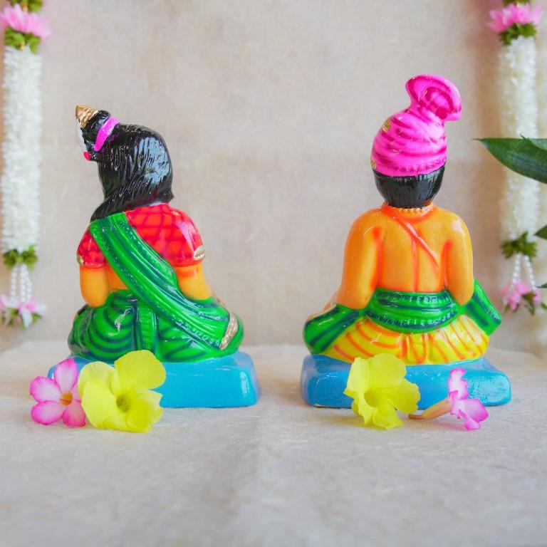 Navarathri Golu dolls depicting a seated Mama and Mami, dressed in traditional attire with vibrant colors, sitting on blue bases.