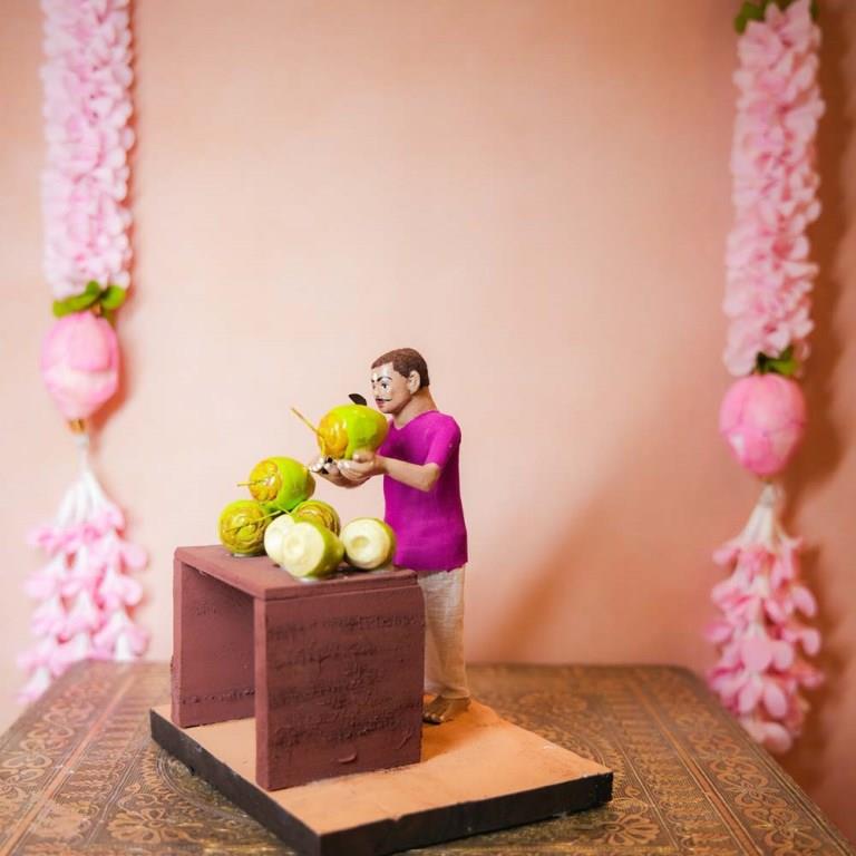 Handcrafted Golu Doll depicting a traditional coconut seller with fresh coconuts on a table, designed for Navarathri Golu.