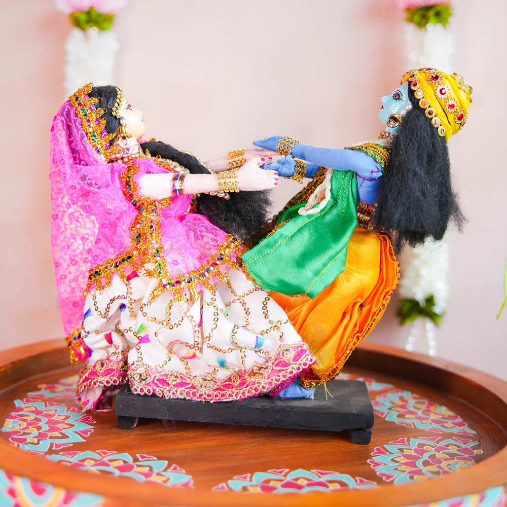 Handcrafted dolls of Radha and Krishna in a playful Raas Leela pose, adorned with vibrant traditional attire and intricate embellishments.