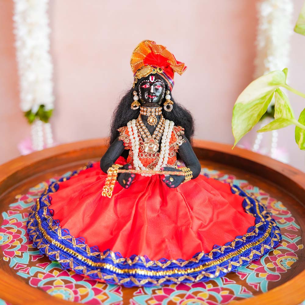 Handcrafted Krishna doll holding a flute, adorned with pearls and ornaments, dressed in vibrant red and blue traditional attire.