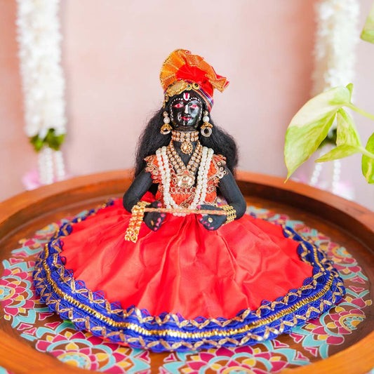 Handcrafted Krishna doll holding a flute, adorned with pearls and ornaments, dressed in vibrant red and blue traditional attire.