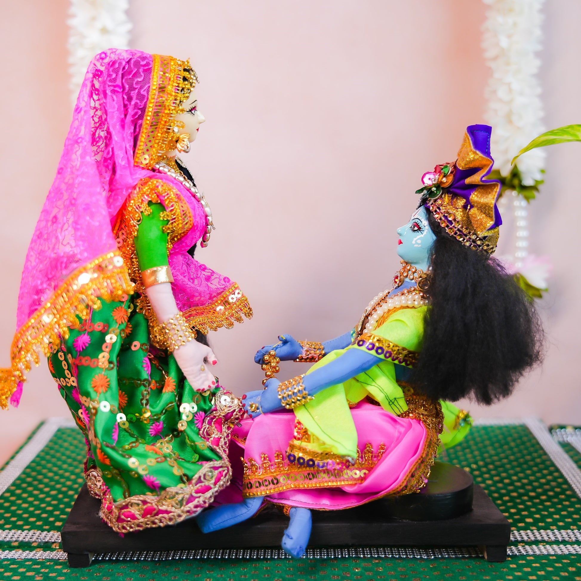Handcrafted dolls of Radha and Krishna in a scene where Radha helps Krishna wear an anklet, dressed in vibrant traditional attire with intricate details.