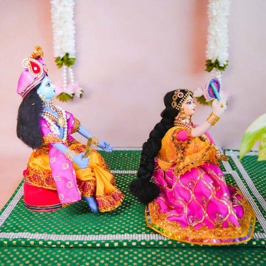Handcrafted costume dolls of Radha combing her hair and Krishna seated beside her, both dressed in vibrant traditional attire.