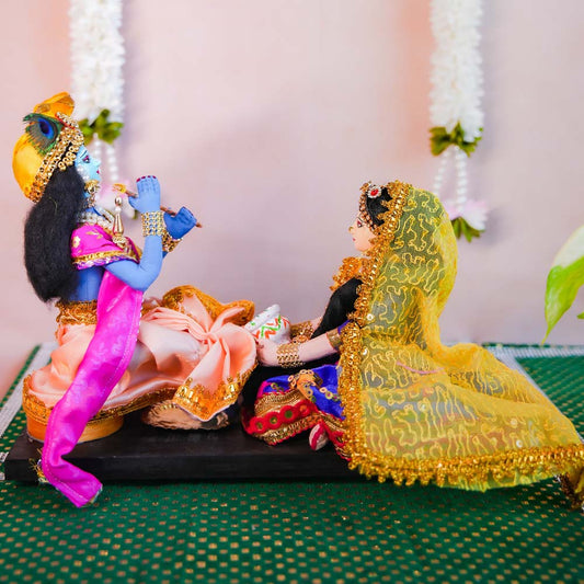 Handcrafted costume dolls of Radha and Krishna in a devotional pose, with Radha washing Krishna's feet, dressed in vibrant traditional attire.