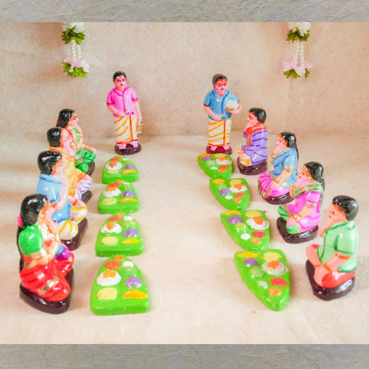 Handcrafted Navaratri Golu Sappadu Set featuring seated figurines enjoying a feast served on banana leaves, vibrantly painted and detailed.
