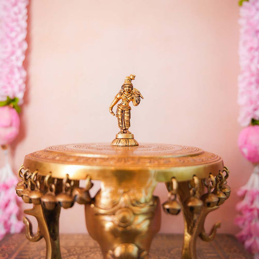 Small brass Andal idol with intricate detailing, displayed on a decorative pedestal.