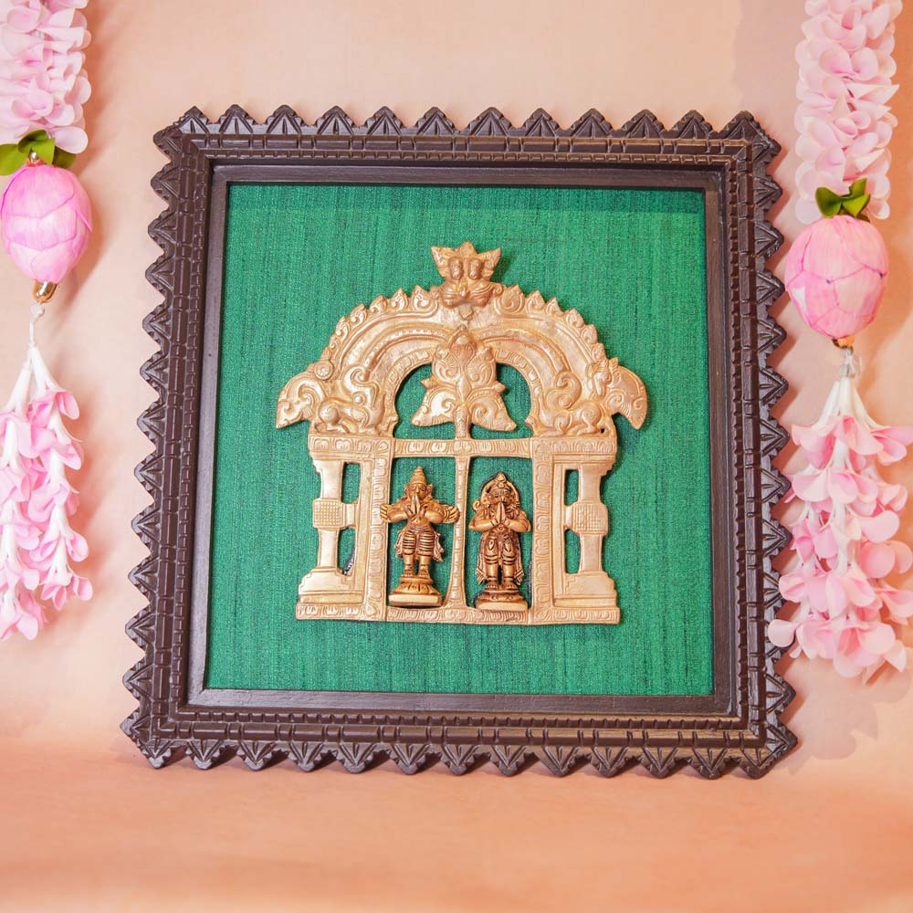 Framed brass sculptures of Hanuman and Garuda within an ornate Prabhavali, mounted on a green fabric background with a carved wooden frame.