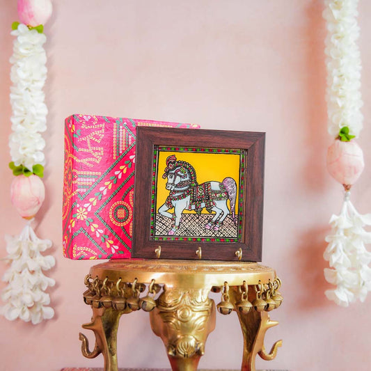 Decorative keyholder featuring a hand-painted Indian horse design on a vibrant yellow background, framed with dark wood, and adorned with key hooks.