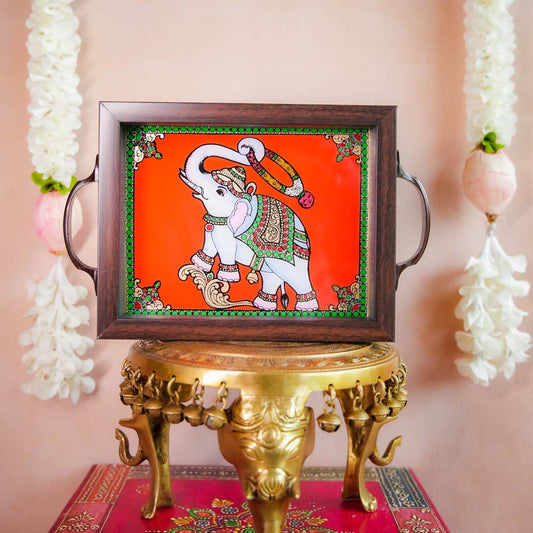 Decorative tray with a hand-painted blessing elephant motif on a vibrant orange background, framed with dark wood and metallic handles, displayed on a traditional brass stand.