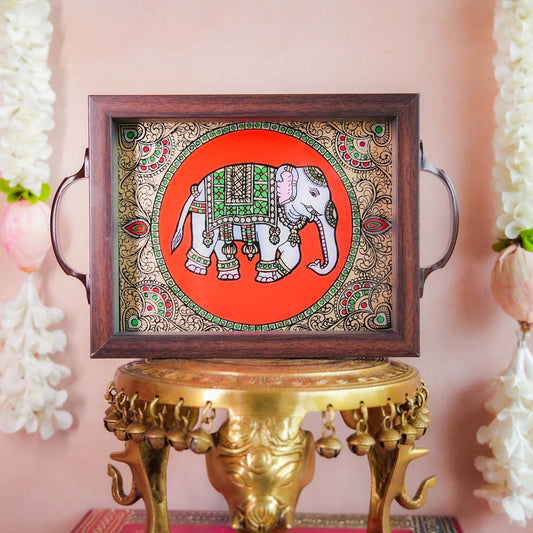 Decorative tray with a hand-painted Indian elephant design on a vibrant orange background, framed with dark wood and metallic handles, displayed on a traditional brass stand.