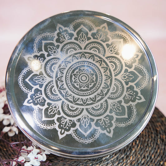 Stainless steel chocolate box with an intricate laser-etched mandala design on the lid, placed on a woven mat with floral decor.