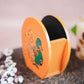 Hand-painted wooden penstand with a vibrant peacock design in green and gold on an orange background.
