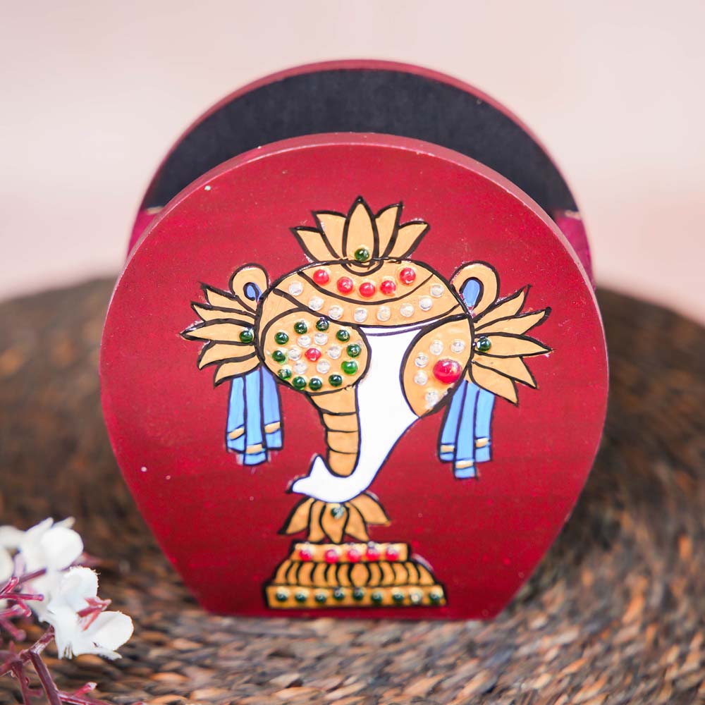 Hand-painted wooden penstand with a traditional conch (Sangu) design in vibrant red, adorned with intricate details and embellishments, placed on a woven mat with floral accents.