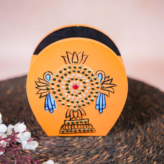 Hand-painted wooden penstand with a vibrant orange Chakram design, embellished with intricate details, placed on a woven mat with floral accents.