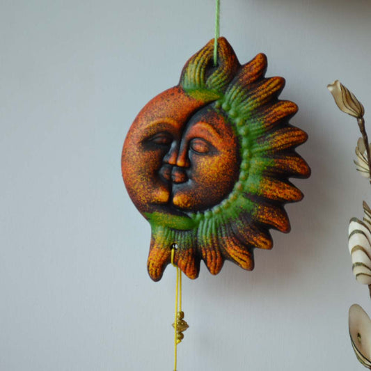 Handcrafted earthen wall hanging featuring sun and moon faces in vibrant earthy tones with a green and orange finish.
