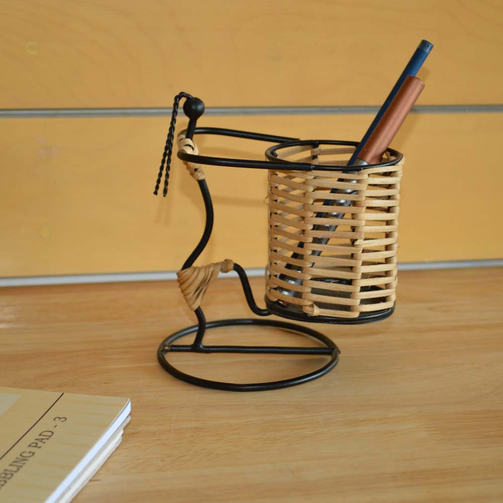 Handcrafted cane pen stand with a black metal base holding pens on a wooden desk.