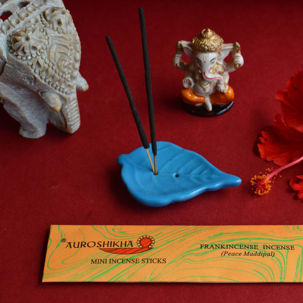 Cera Leaf Blue Ceramic Incense Holder with Auroshikha Frankincense Mini Sticks gift set, featuring a Ganesha figurine, an intricately carved elephant, and a red hibiscus flower on a red backdrop.