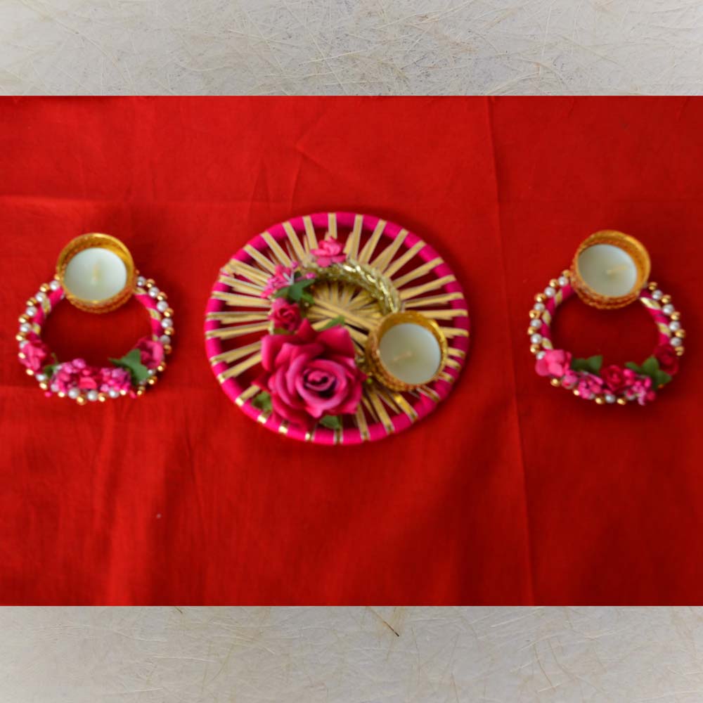 Fancy pink and gold T-light diya set featuring a circular centerpiece with golden leaf designs and two smaller T-light holders adorned with pearls and flowers.