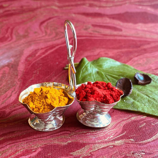 Silvery dual haldi kumkum cup with floral design and connecting handle, perfect for pooja rituals and festive decor.