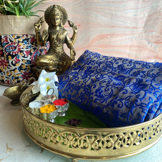 Banaras royal blue brocade fabric with floral motifs, displayed with traditional brass decor and festive accessories.