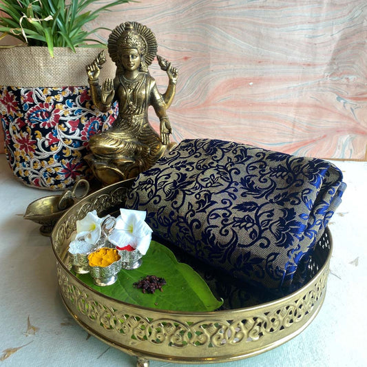 Banaras dark blue brocade fabric with golden floral motifs, beautifully displayed with traditional brass decor and festive accents.