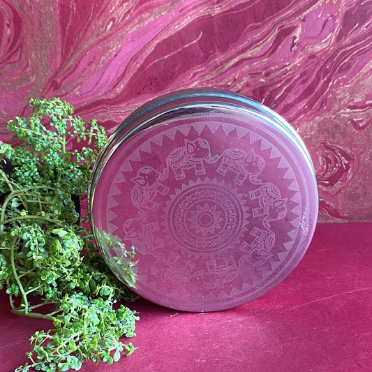 Round glass food container with an engraved elephant mandala design, placed against a pink and gold textured background.