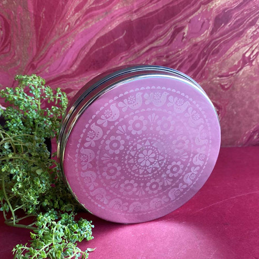 Round glass food container with an etched paisley and bird design, placed against a pink and gold textured background.