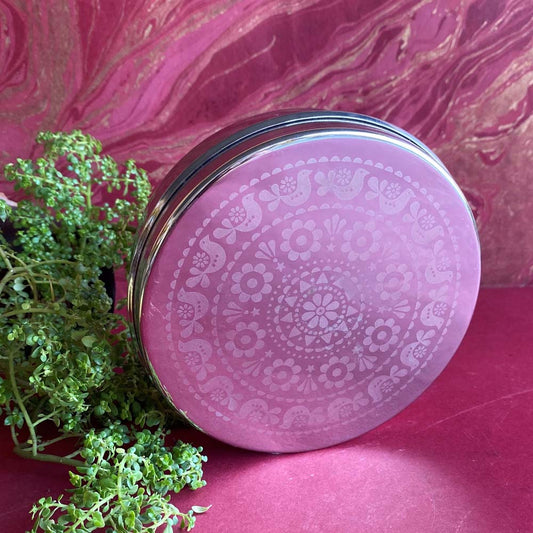 Circular stainless steel food container with an etched bird and floral design on the lid, size 6, displayed on a red background with greenery.
