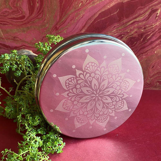 Round glass food container with an intricately etched floral mandala design, placed against a pink and gold textured background.