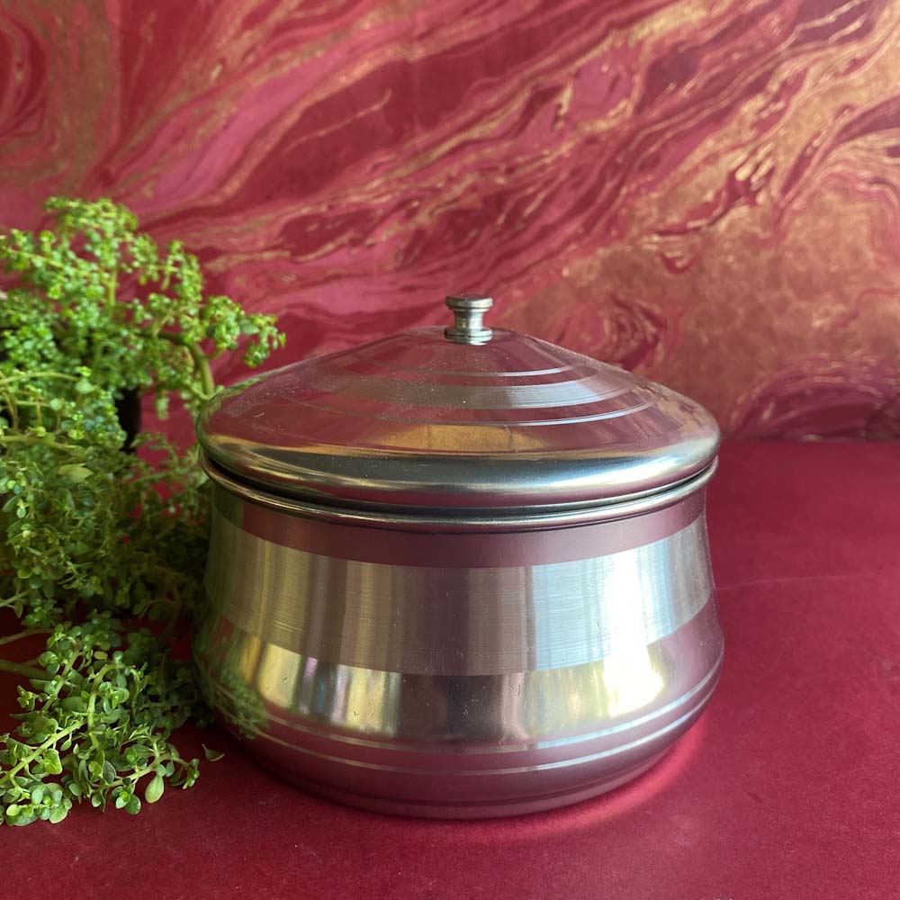 Stainless steel serving and storing dish with a polished lid, placed against a pink and gold textured background.