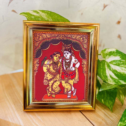Tanjore-style framed artwork featuring Radha and Krishna standing together, set against a vibrant red backdrop, adorned with intricate detailing and enclosed in a golden frame.