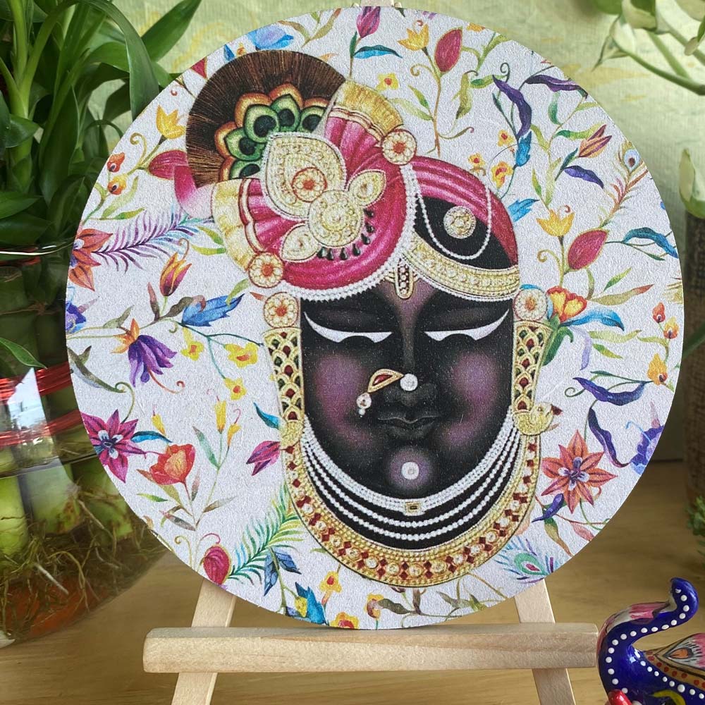 Decorative plate featuring the face of Shreenathji adorned with intricate jewelry and vibrant floral patterns, set on a white background and displayed on a wooden easel.