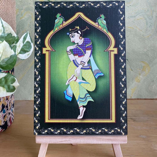 Decorative artwork of a village lady in vibrant blue and green attire, framed by a minaret-style arch with intricate detailing, displayed on a wooden easel.
