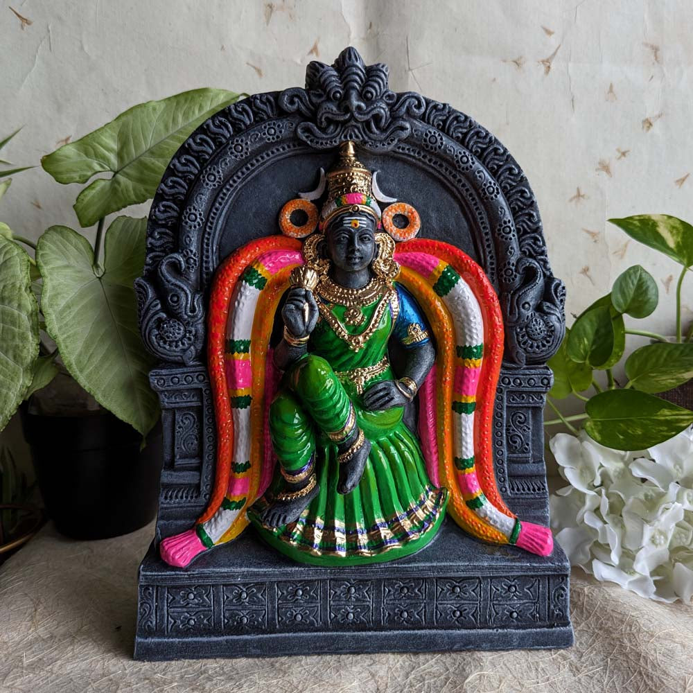 Kamalambal (Kamalambigai) Golu doll seated within a black temple frame, dressed in a green saree and adorned with vibrant garlands and ornaments.