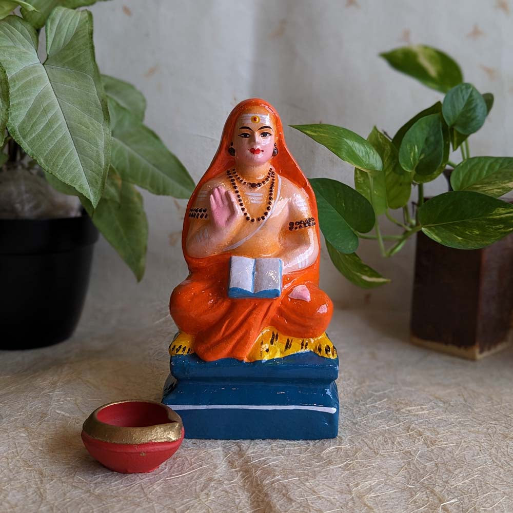 Hand-painted small Adi Shankaracharya Golu doll in orange, seated with scriptures, ideal for Navarathri decoration.