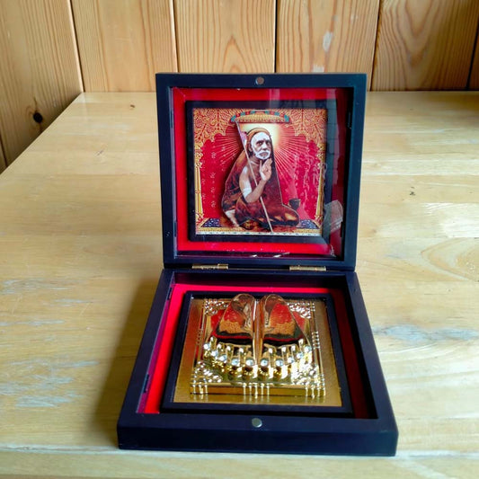 Compact Mahaperiyava Padhuka set in a black-framed box with a golden representation of holy feet and a vibrant framed image of Mahaperiyava in the background.