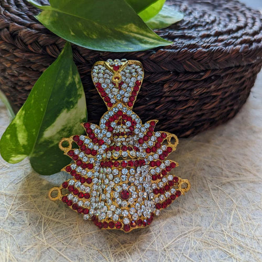Gold-plated crown-shaped pendant with red and white stones on a woven and leafy background.