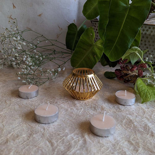 Handcrafted gold basket-style tealight holder surrounded by tealights and natural greenery.