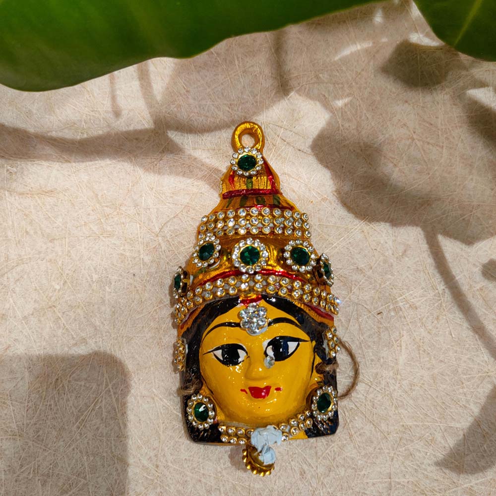 Handcrafted small Amman Face decor with jeweled crown, adorned with crystals and green accents, displayed against a textured background.